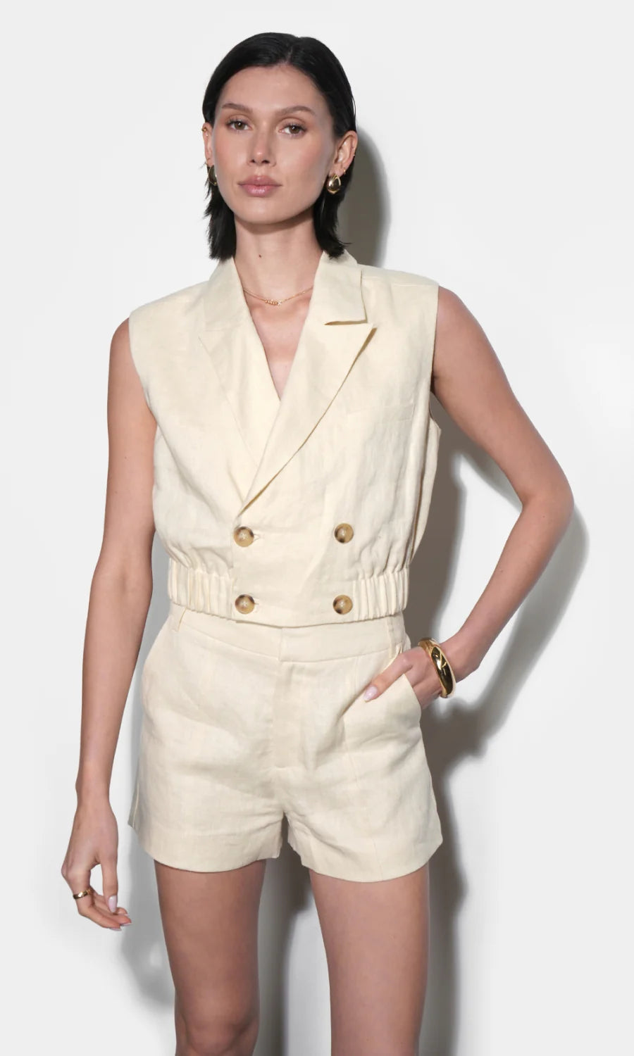 Woman wearing a cream-colored sleeveless blazer and shorts set against a white background