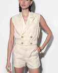 Woman wearing a cream-colored sleeveless blazer and shorts set against a white background