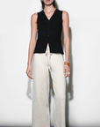 Woman wearing a black sleeveless vest and white pants against a white background