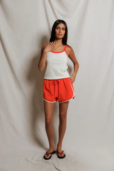 Woman wearing a white tank top with orange trim and orange shorts against a plain background
