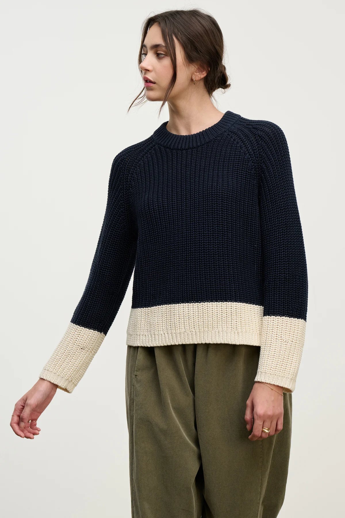 Person wearing a navy sweater with beige cuffs and hem on a white background