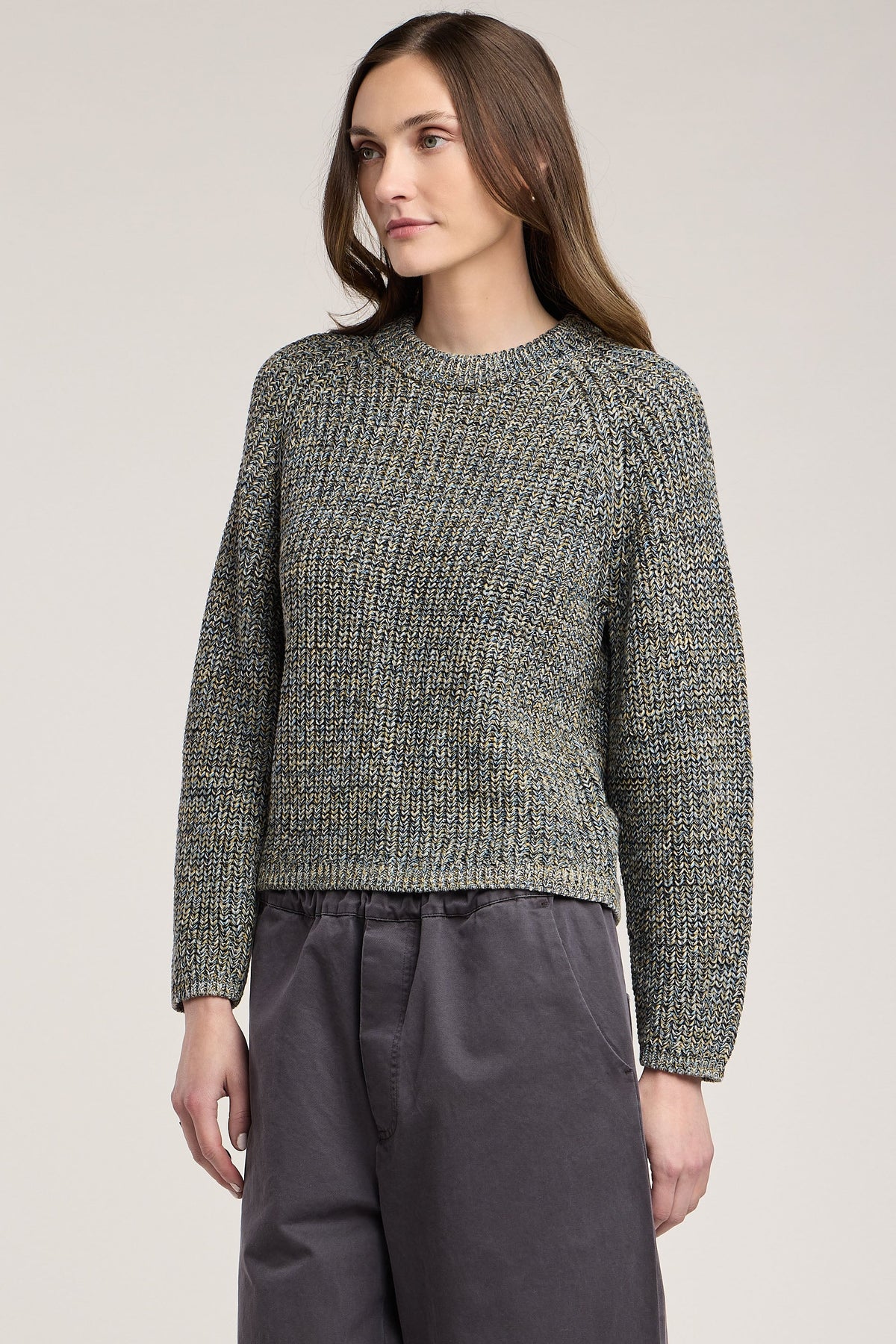 Woman wearing a textured sweater and dark pants on a plain background