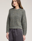 Woman wearing a textured sweater and dark pants on a plain background