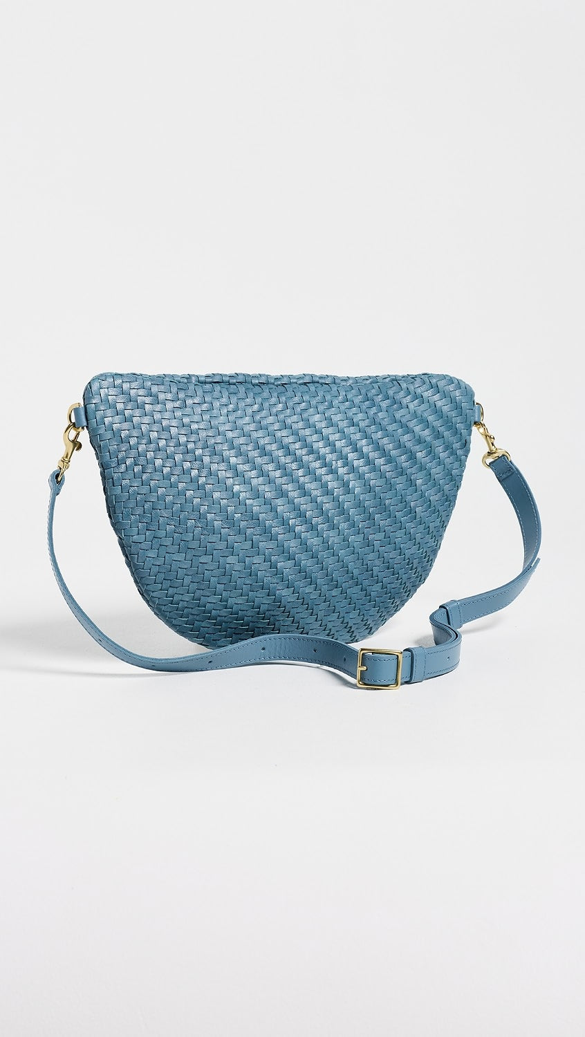 A blue woven leather crescent-shaped shoulder bag with a matching adjustable shoulder strap and gold-tone hardware, photographed on a clean white background.