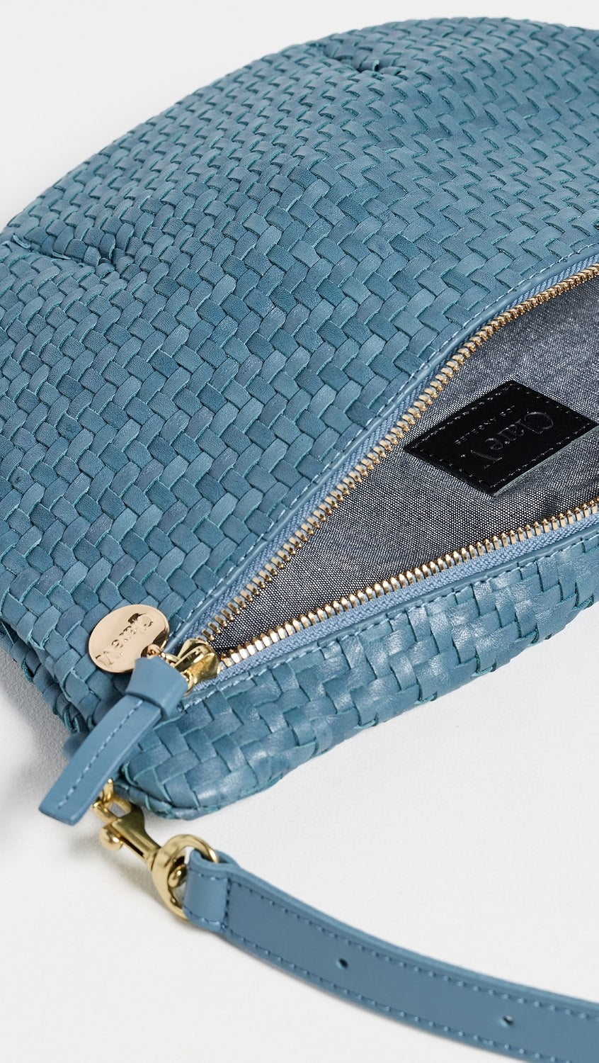 A close-up of a woven blue leather shoulder bag with gold-tone hardware, a zippered compartment, and a matching blue leather strap on a white background.