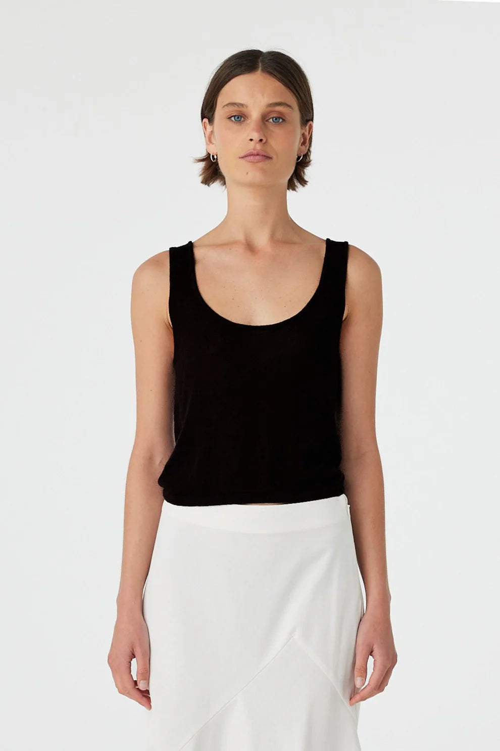 Woman wearing a black tank top and white pants on a plain background