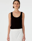 Woman wearing a black tank top and white pants on a plain background