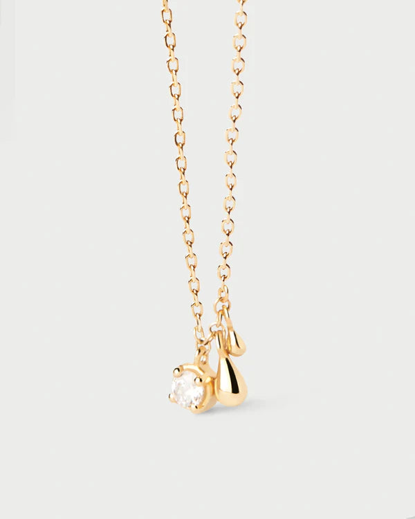 Gold necklace with a small pendant on a light gray background detail view