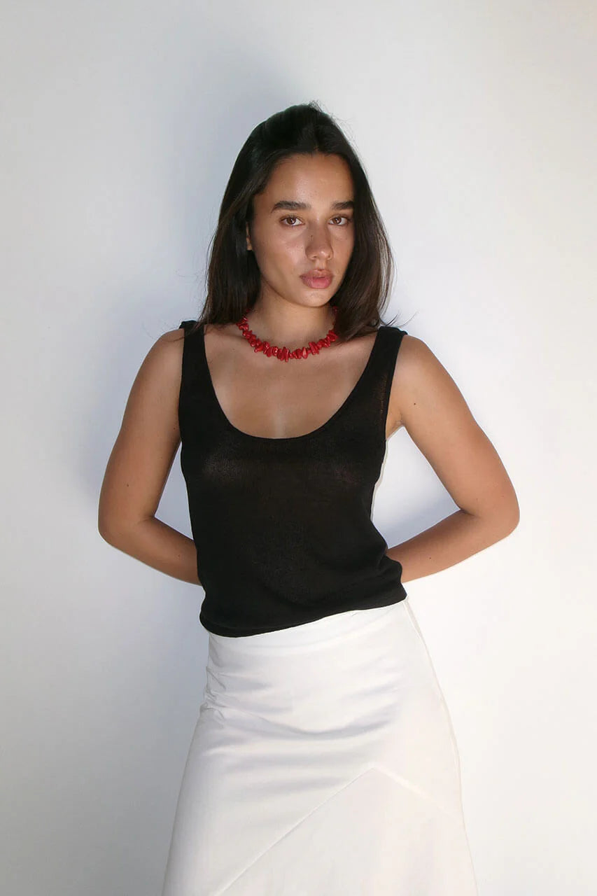 Woman wearing a black top and white skirt with a red necklace against a plain background