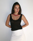 Woman wearing a black top and white skirt with a red necklace against a plain background
