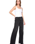 Woman wearing a white tank top and black wide-leg jeans on a white background