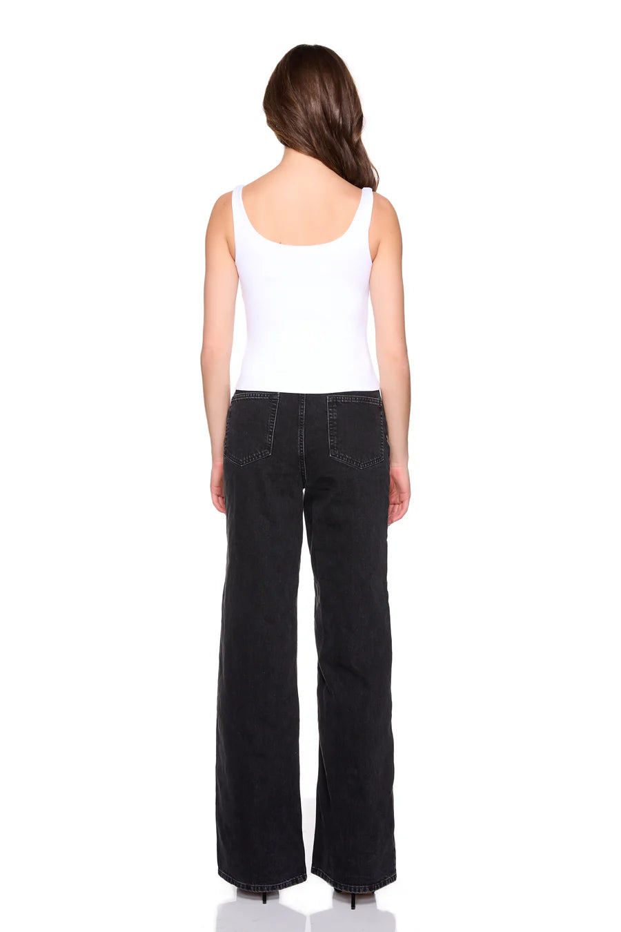 Person wearing a white tank top and black flared jeans on a white background, back view