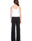 Person wearing a white tank top and black flared jeans on a white background, back view