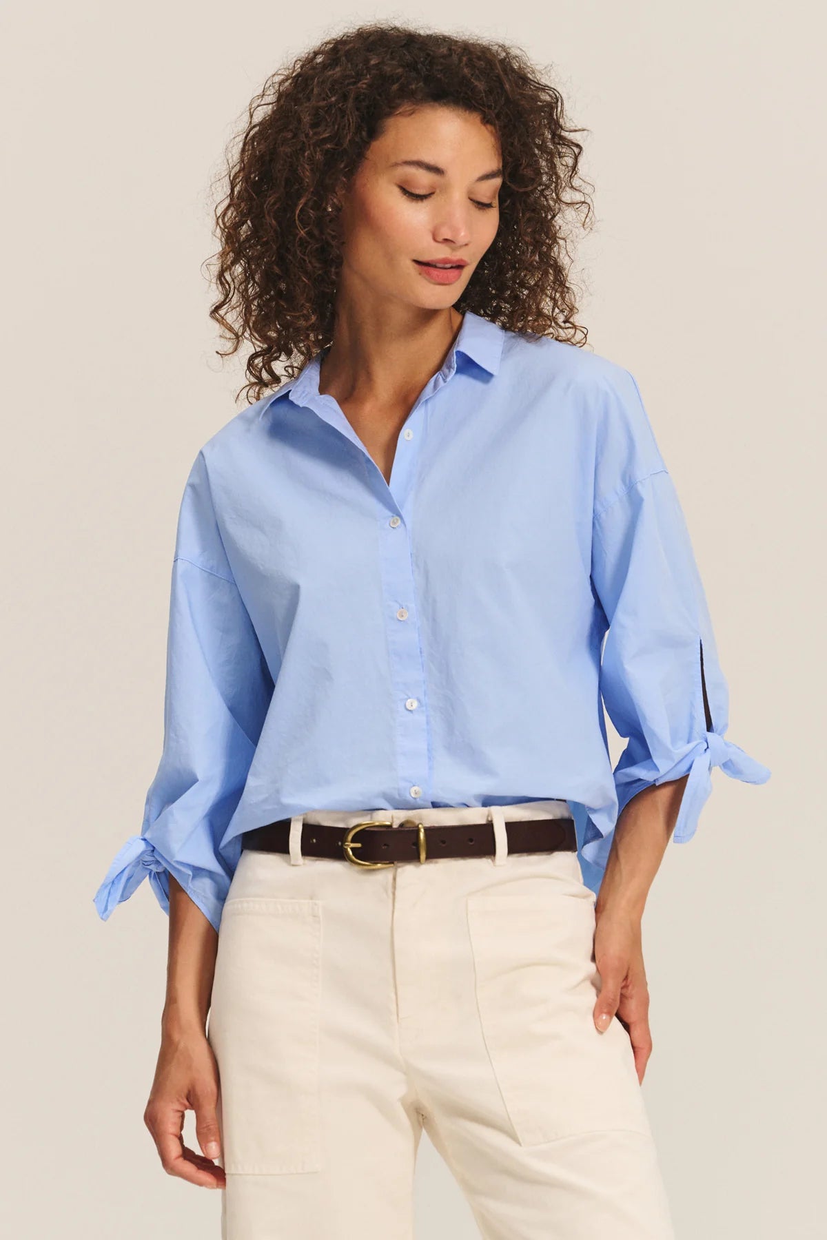 Woman wearing a light blue shirt and beige pants on a plain background