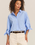 Woman wearing a light blue shirt and beige pants on a plain background