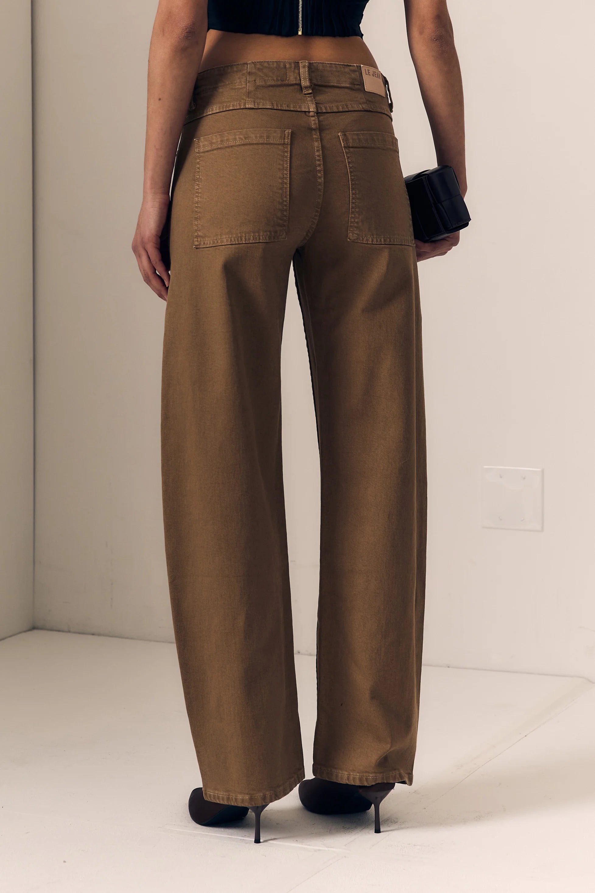 A person shown from the back wearing wide-leg brown pants, a black crop top, and black heels, standing in a plain indoor setting.