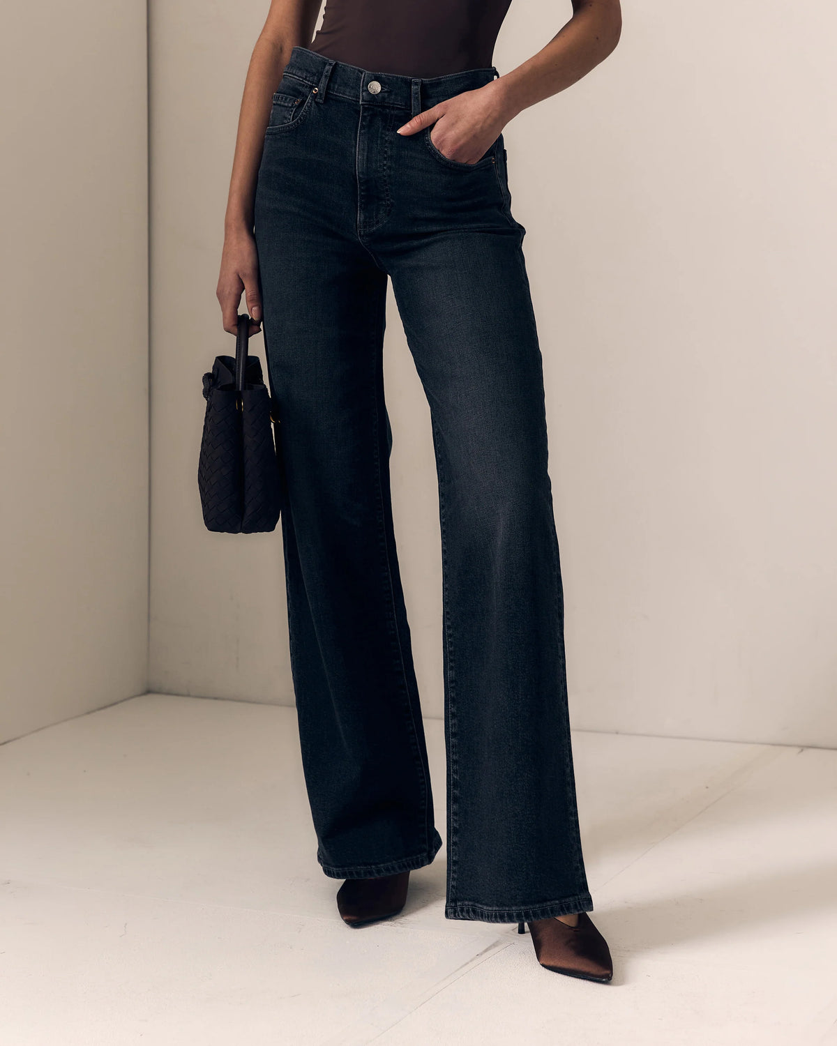 model wearing a strapless brown top with dark jeans on a cream background 