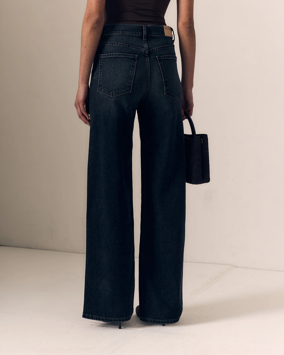 model wearing a strapless brown top with dark jeans on a cream background, back view 