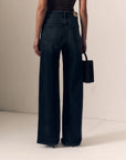 model wearing a strapless brown top with dark jeans on a cream background, back view 