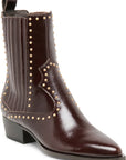 A dark brown leather ankle boot with gold-tone metal studs, featuring a pointed toe, low block heel, and a pull tab at the top, shown against a plain white background.