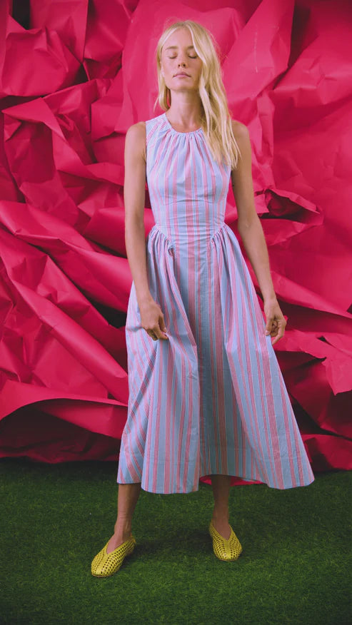 Woman in a striped dress standing against a pink abstract background