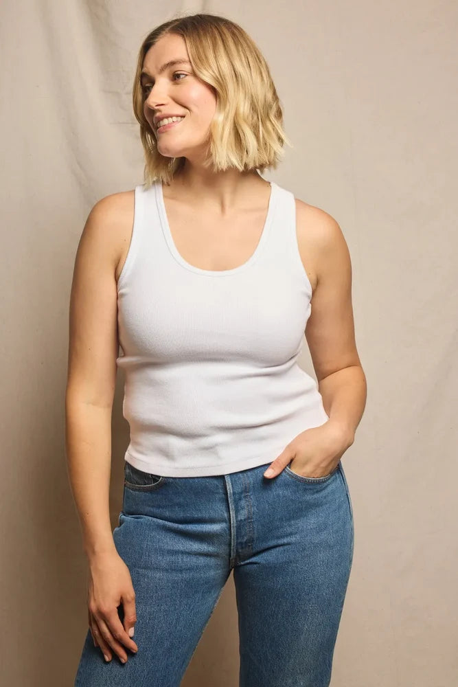 Woman size L wearing a white tank top and blue jeans against a beige background