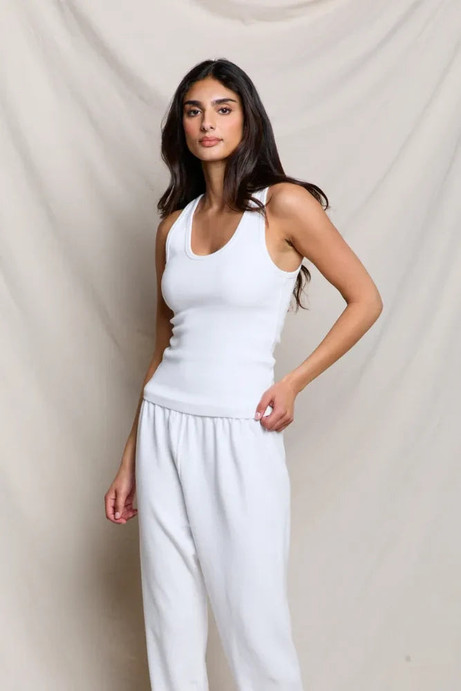 Woman wearing a white tank top and pants against a beige background