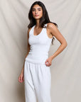 Woman wearing a white tank top and pants against a beige background
