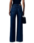 Rear view of a model wearing dark blue wide-leg jeans with a black top and holding a black handbag against a white background.