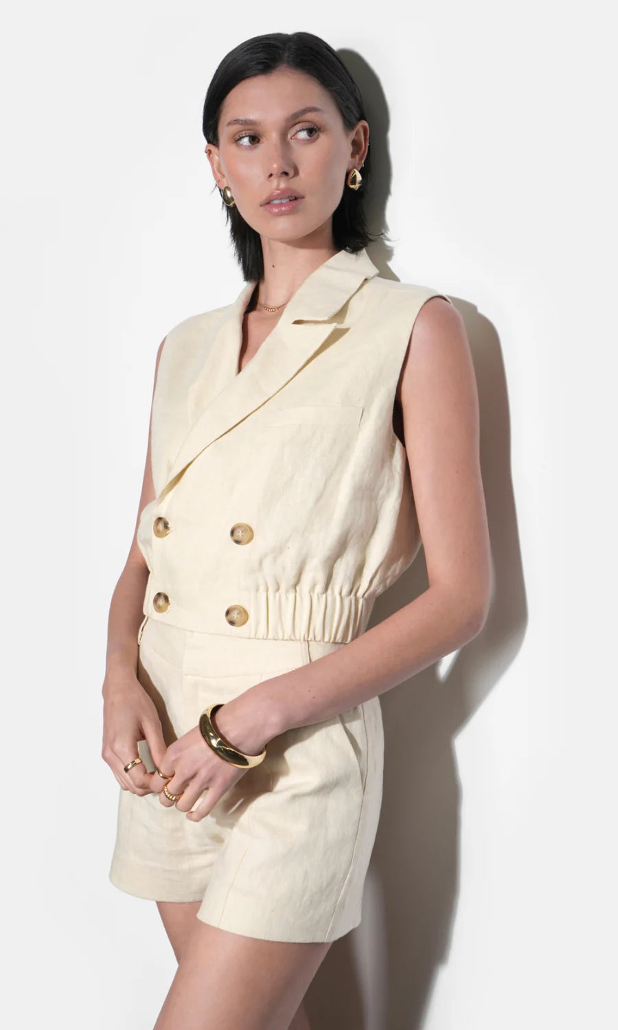 Woman wearing a cream-colored sleeveless blazer dress against a white background