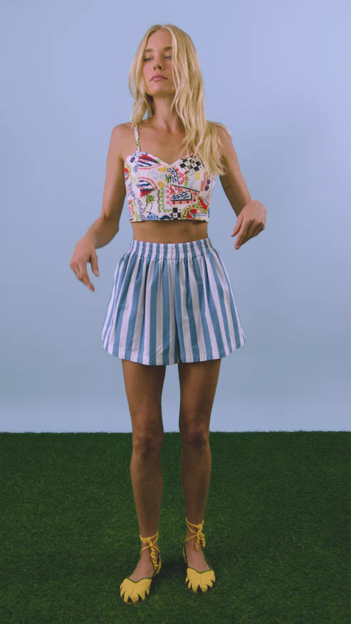 Woman wearing a floral top and striped skirt on a grassy surface with a blue background