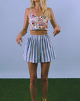 Woman wearing a floral top and striped skirt on a grassy surface with a blue background