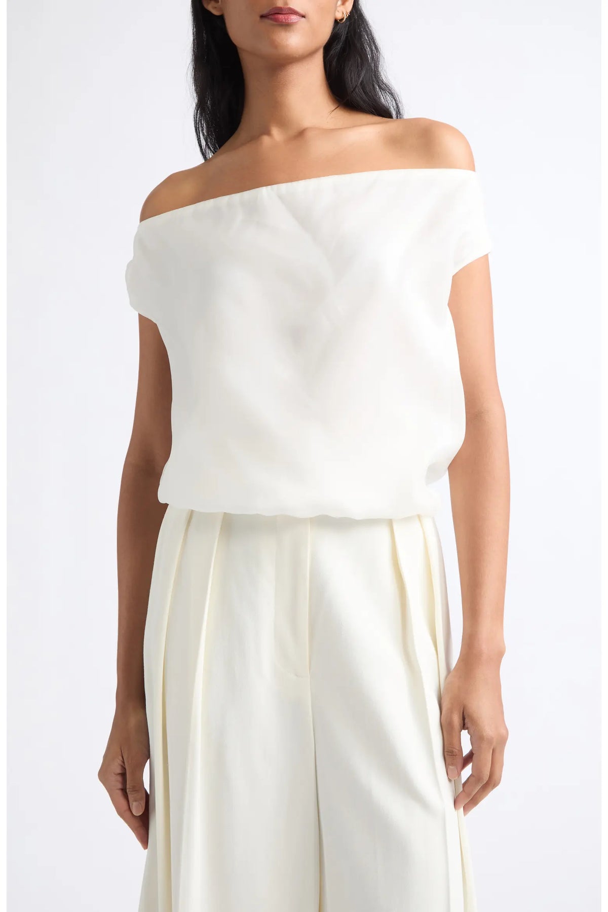 An off-the-shoulder cream-colored top worn by a model, paired with matching cream wide-leg trousers, against a plain white studio background.