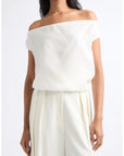An off-the-shoulder cream-colored top worn by a model, paired with matching cream wide-leg trousers, against a plain white studio background.