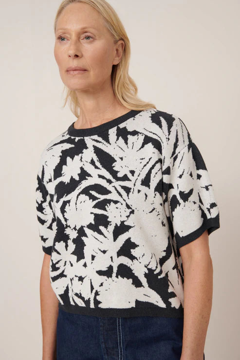 Woman wearing a black and white floral patterned top against a plain background