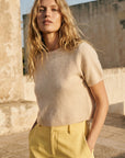 Woman wearing a beige sweater and yellow pants standing outdoors.