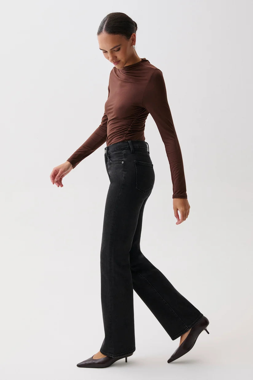 A woman modeling a dark brown ruched long-sleeve top and black wide-leg jeans against a plain light gray studio background.
