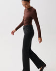 A woman modeling a dark brown ruched long-sleeve top and black wide-leg jeans against a plain light gray studio background.
