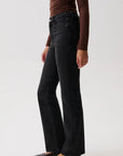 A model wearing black wide-leg flare jeans, a brown long-sleeve top, and dark brown pointed-toe flats, shown from the waist down against a light gray studio background.