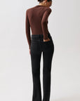 A model shown from the back wearing a brown long-sleeve top, black flare jeans, and dark pointed-toe heels against a plain light gray studio background.