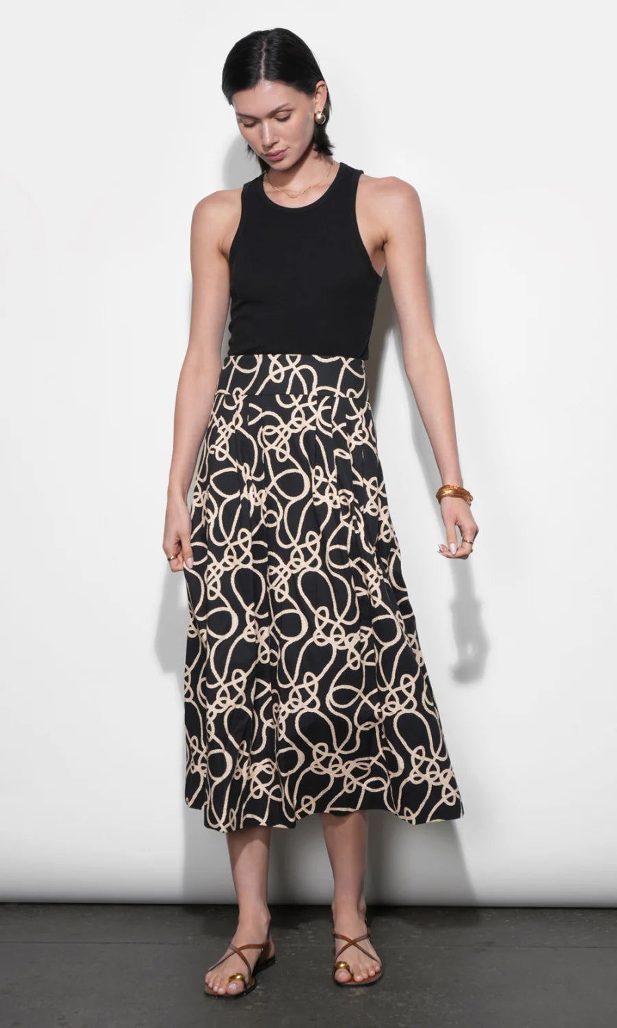 Woman wearing a black sleeveless top and patterned skirt against a white background