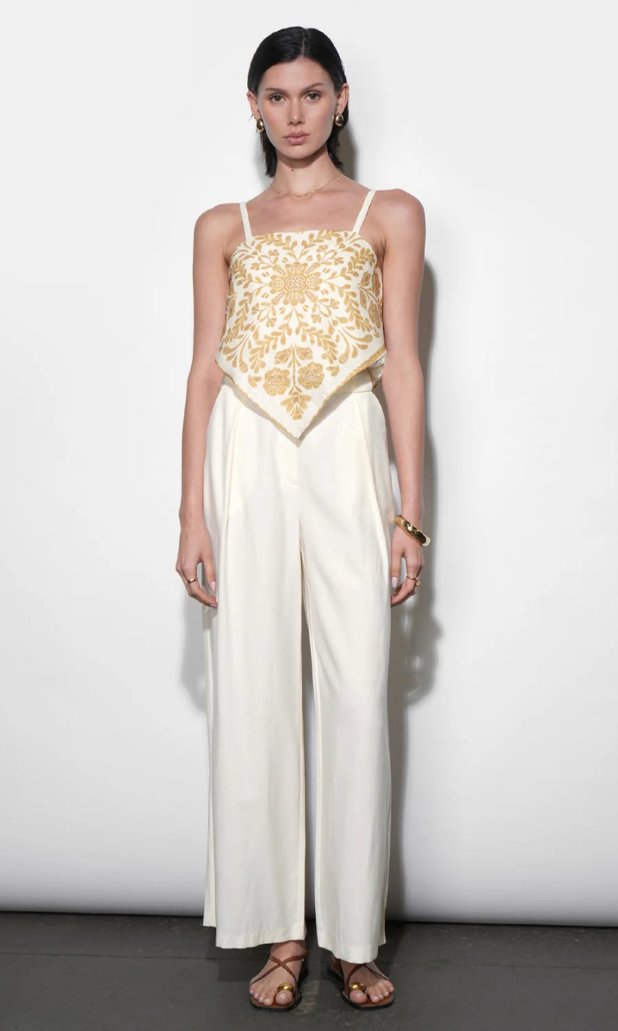Woman wearing a white outfit with gold lace top against a white background