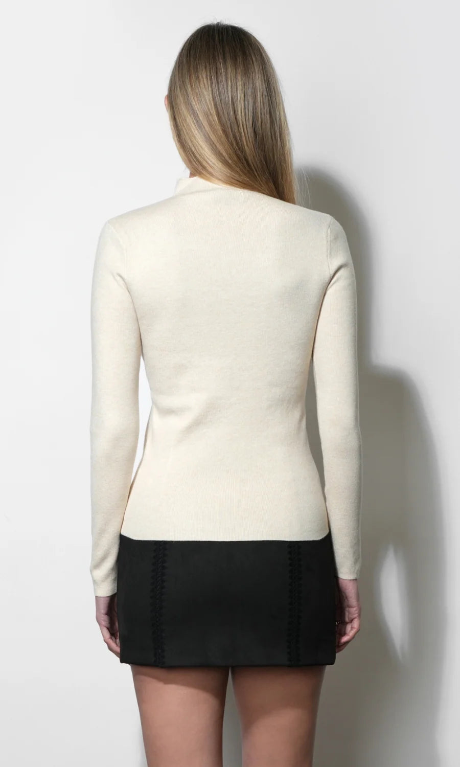 woman wearing a cream long sleeve top with a black mini skirt on a white background, back view