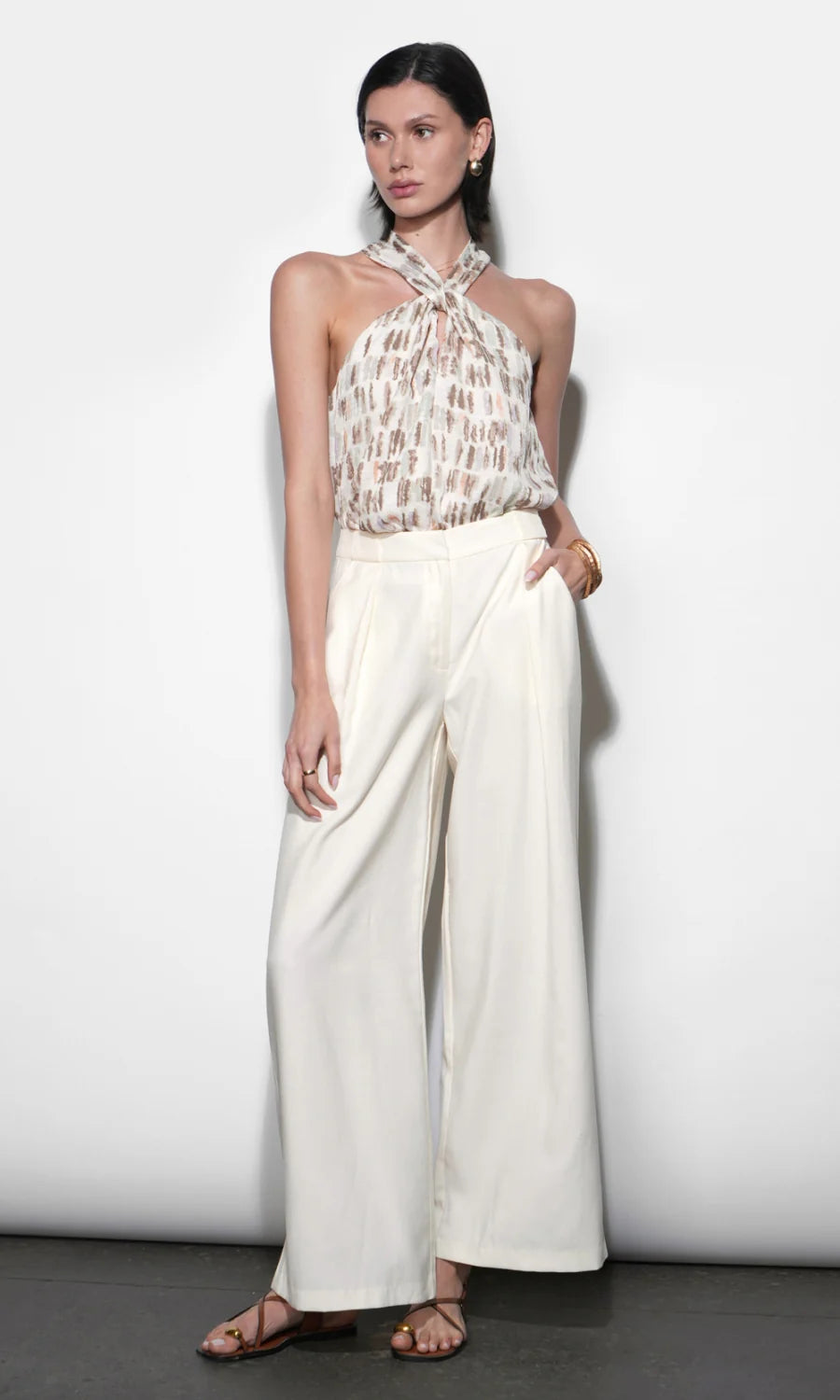 Woman wearing a patterned top and white wide-leg pants against a plain background