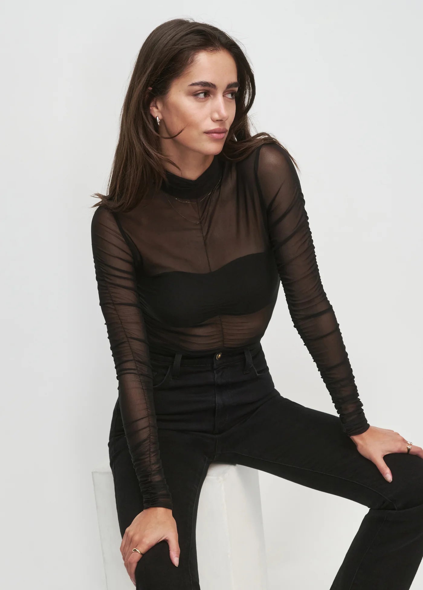 Woman wearing a black sheer long-sleeve top and black pants against a white background