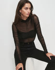 Woman wearing a black sheer long-sleeve top and black pants against a white background