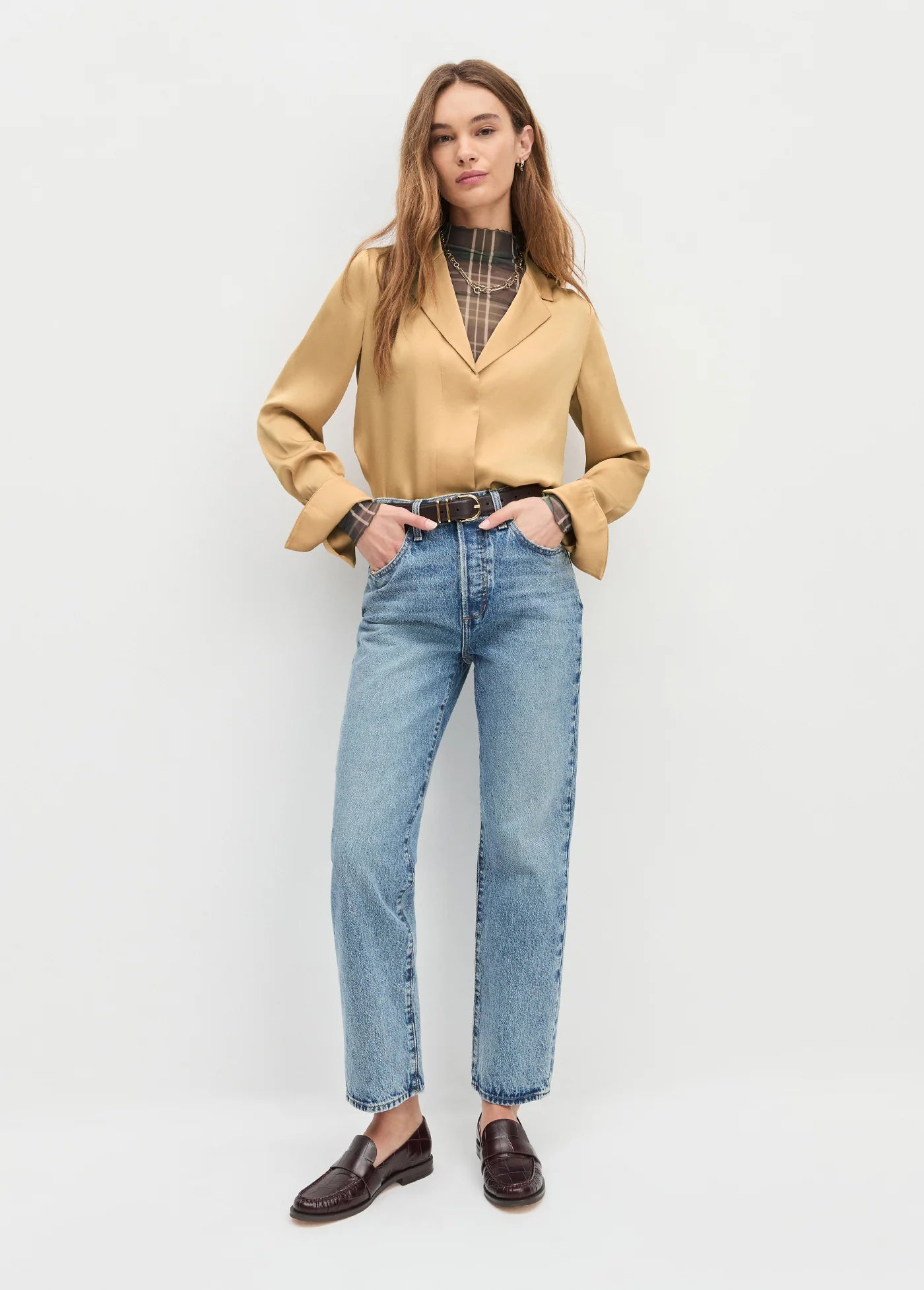 Woman wearing a beige blazer, plaid shirt, and blue jeans on a white background