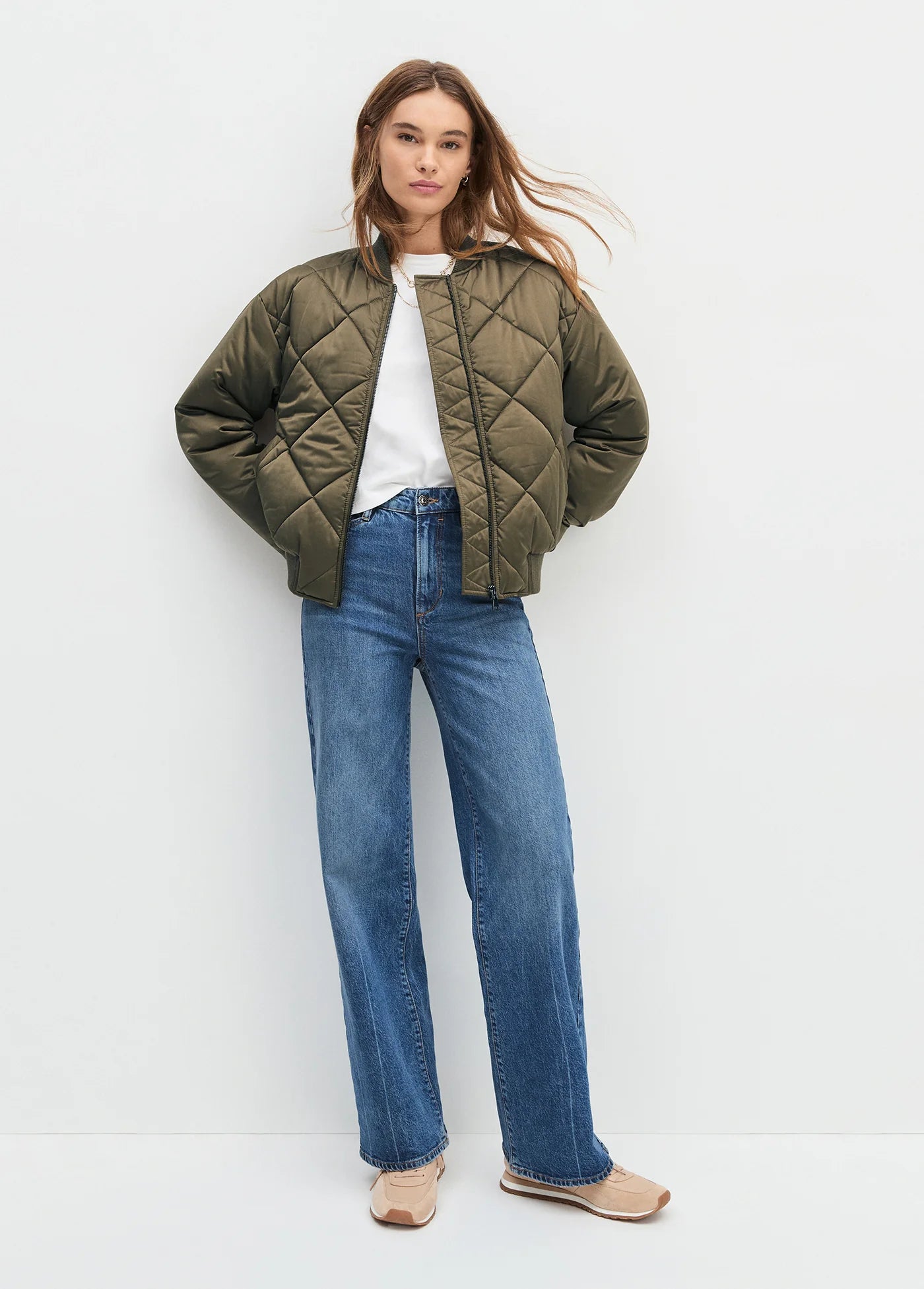 Person wearing a green quilted jacket and blue jeans on a white background