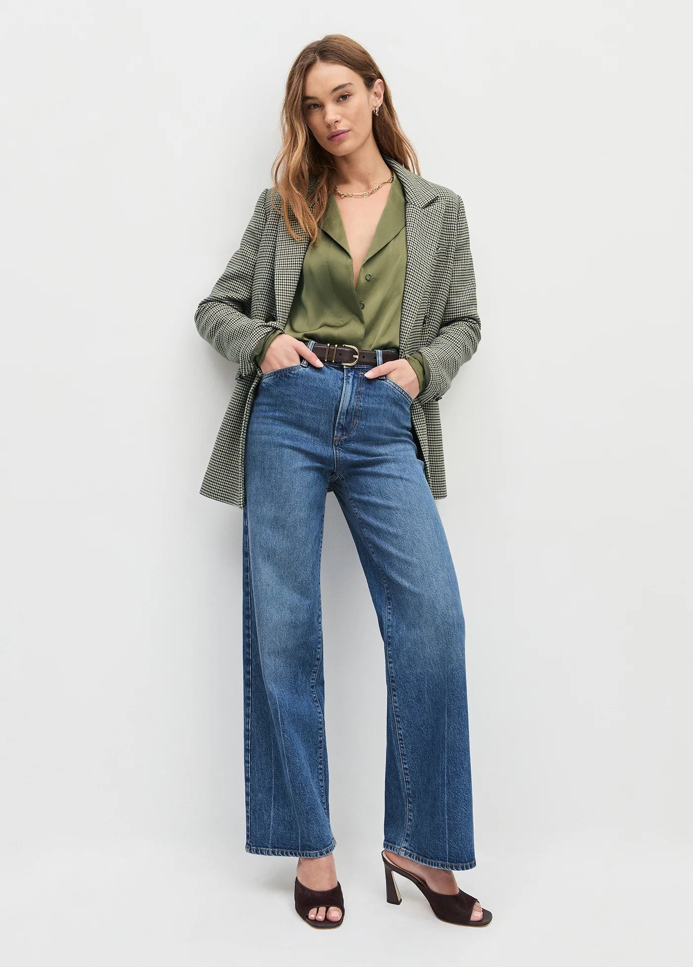 Woman wearing a green blazer, green top, and blue jeans on a white background