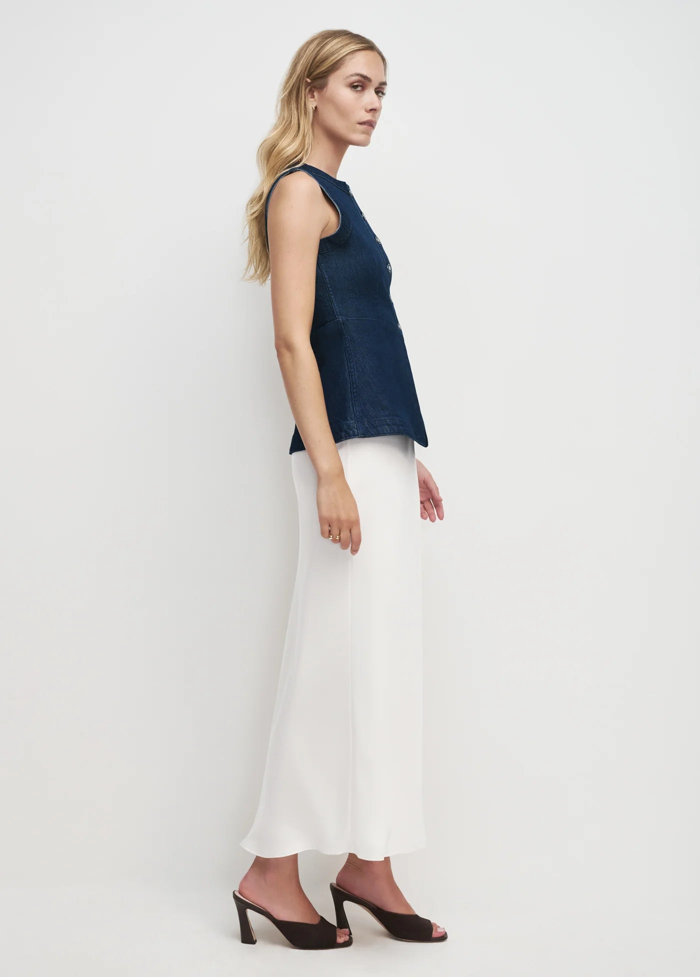 Woman wearing a navy sleeveless top and white pants on a plain background